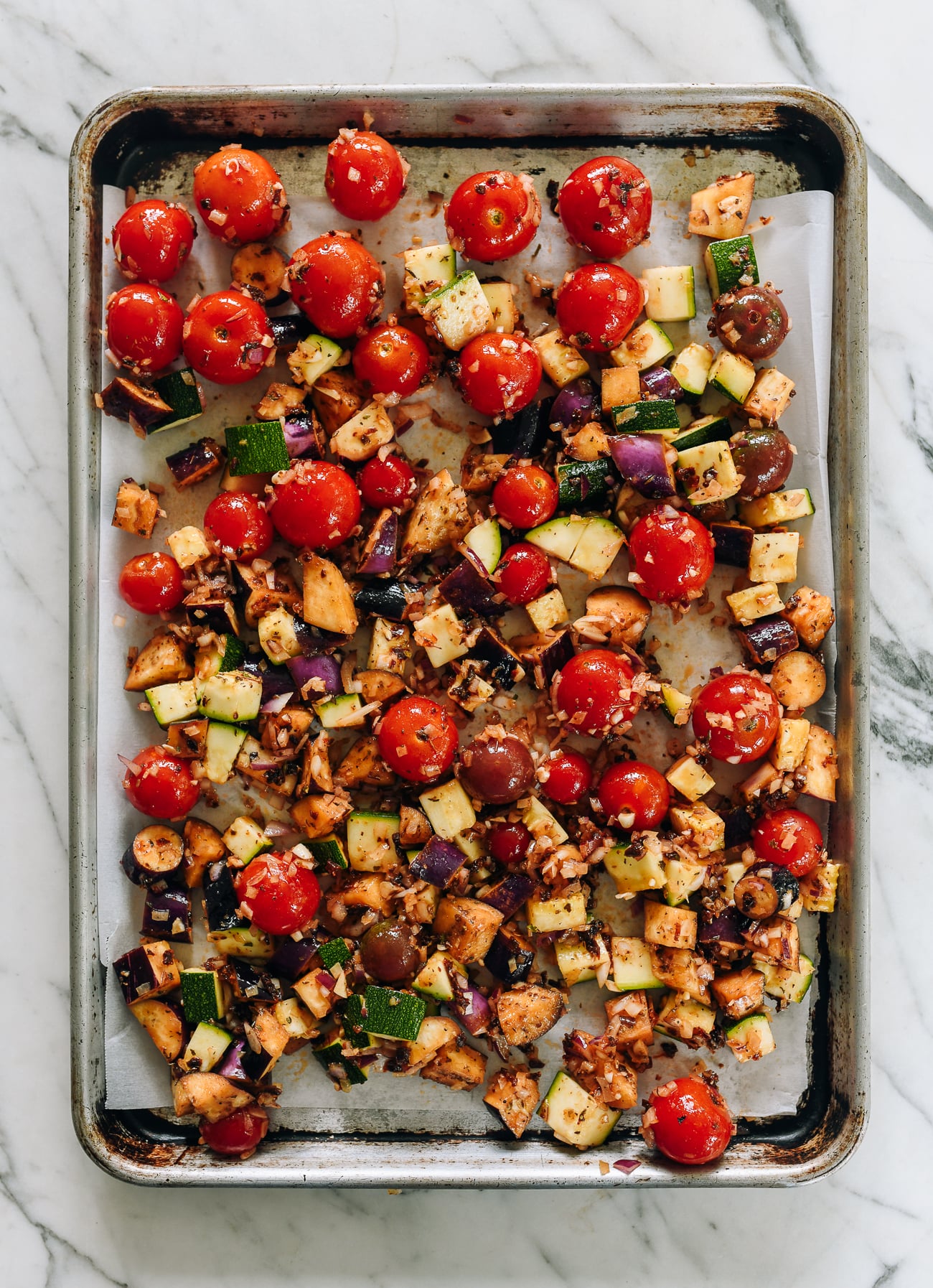 parchment lined sheet pan with seasoned tomatoes, zucchini, and eggplant