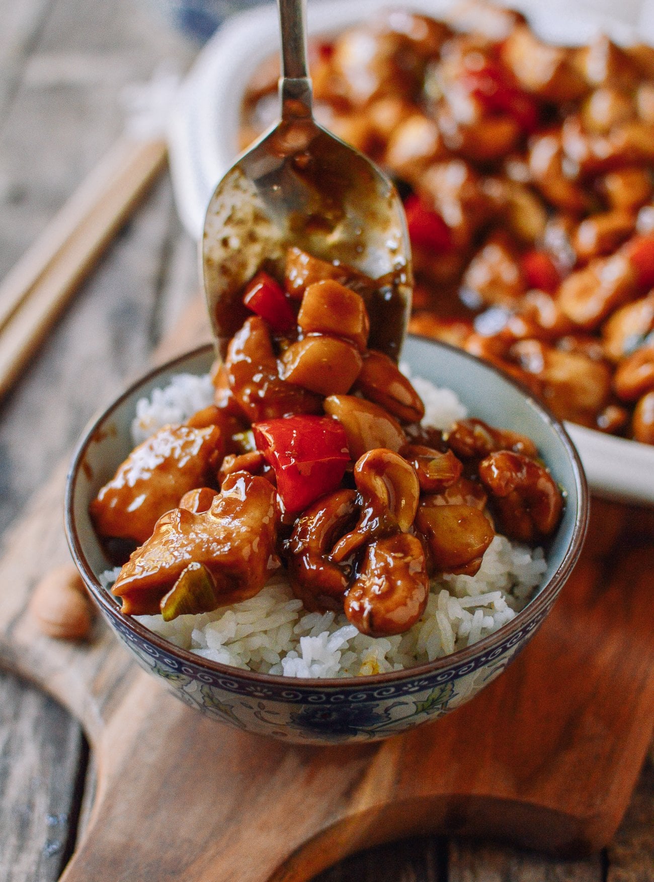 Scooping cashew chicken stir-fry over bowl of steamed rice