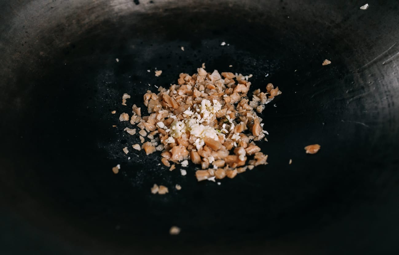 Adding preserved radish and garlic to oil in wok