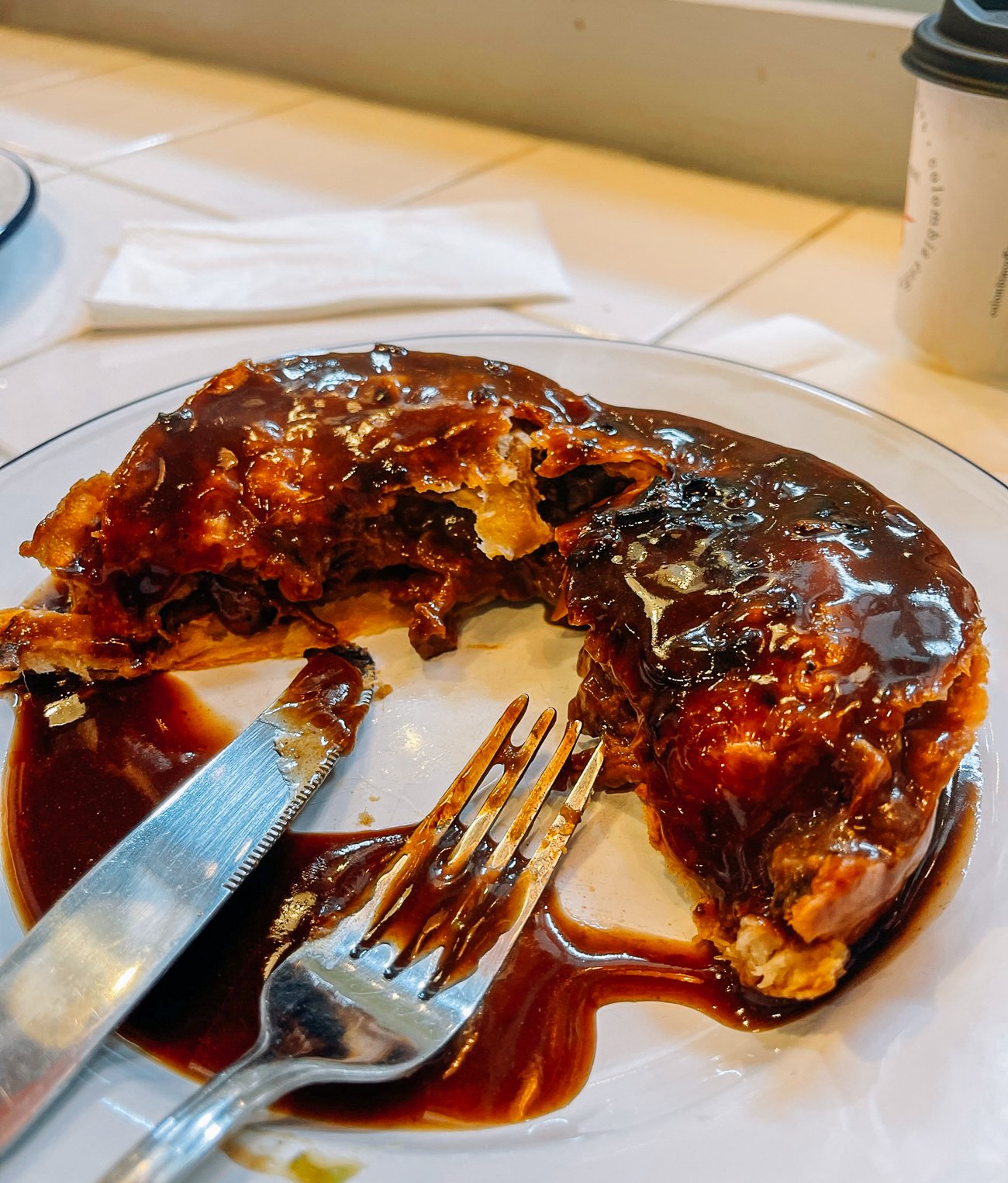 Steak and Ale pie, cut in half with dark brown gravy and a fork and knife