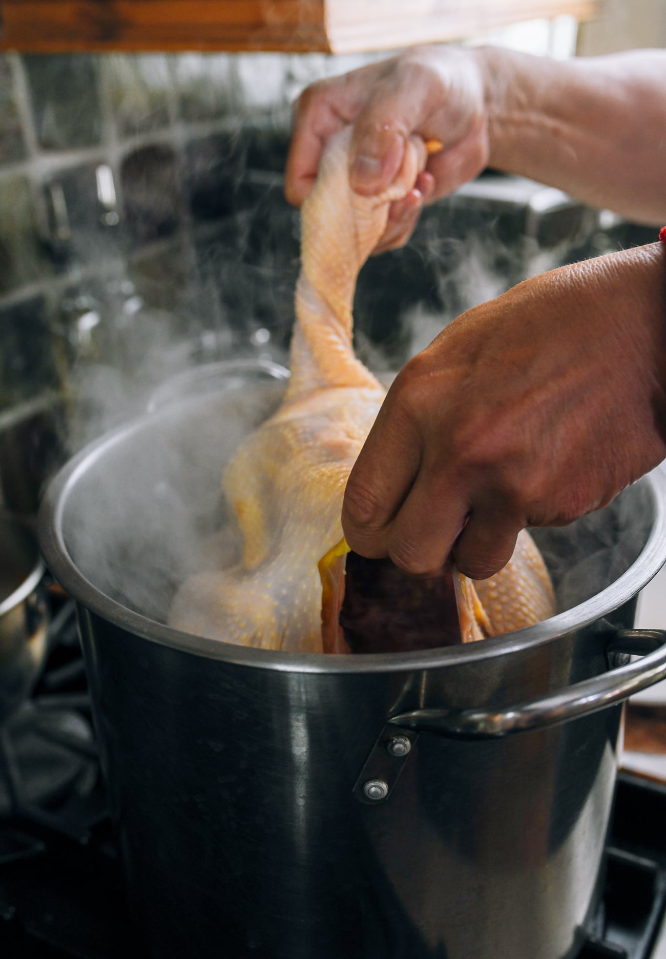 lowering whole buddhist-style Chinese chicken into pot of boiling water