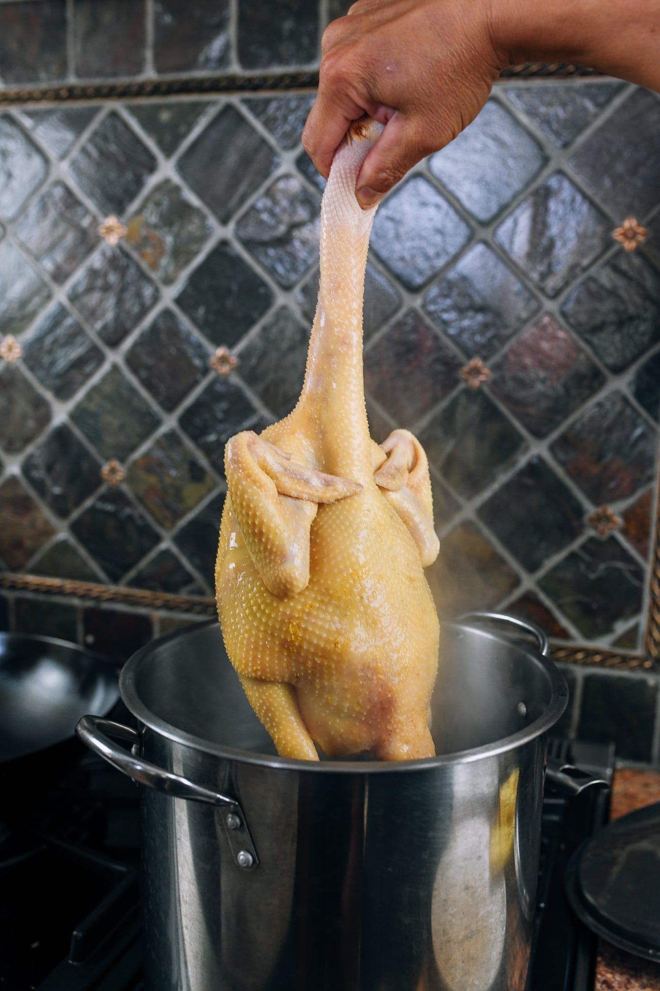 pulling head-on chicken out of poaching liquid to release cold water in cavity