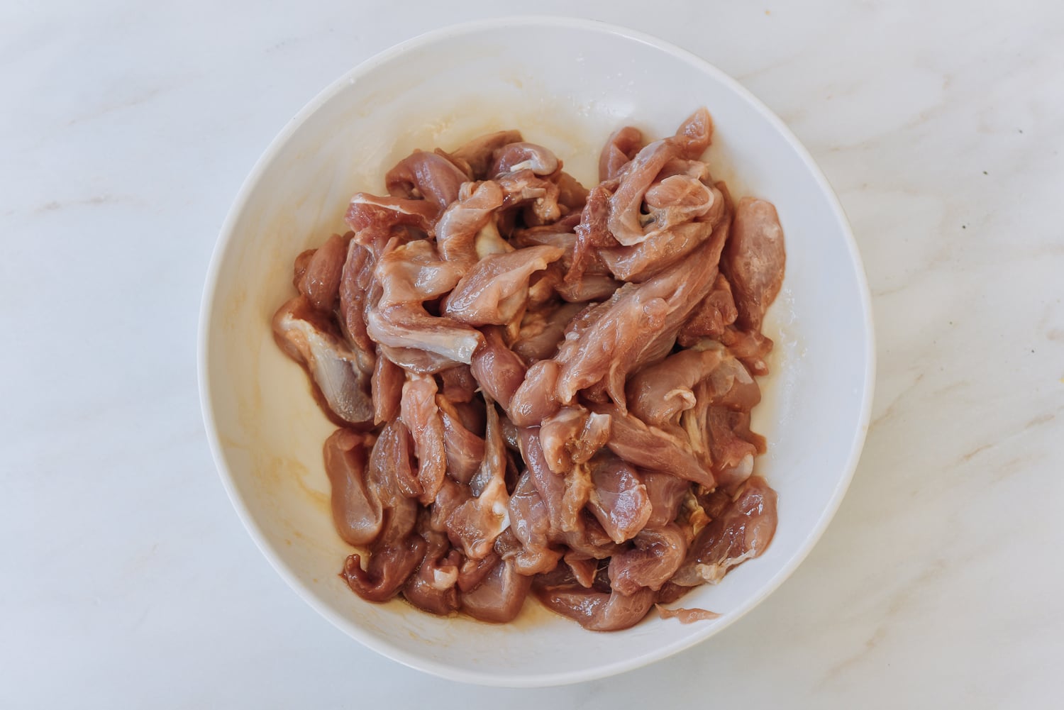 marinated strips of boneless skinless chicken thigh in white dish