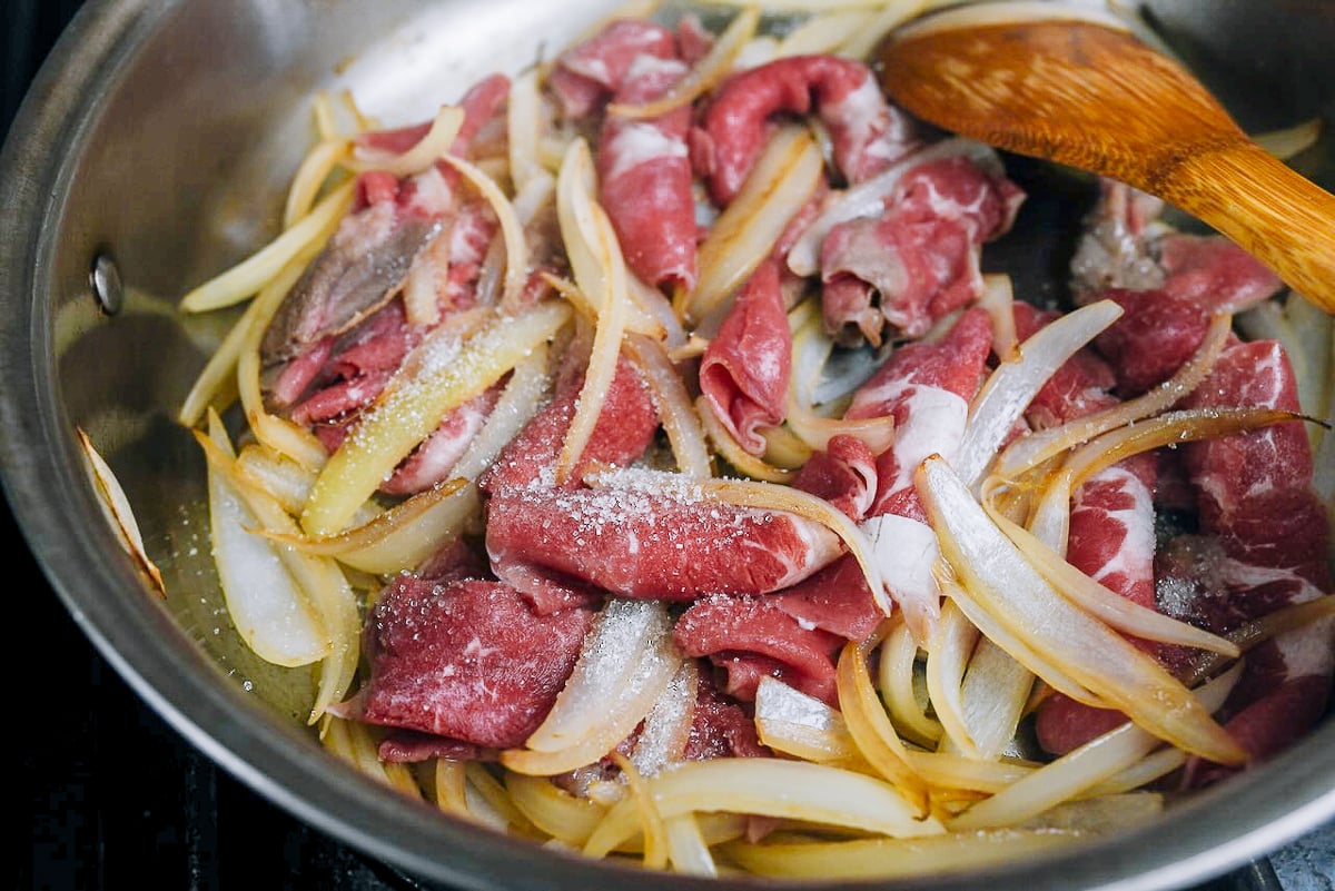 cooking thinly shaved beef and onion in skillet