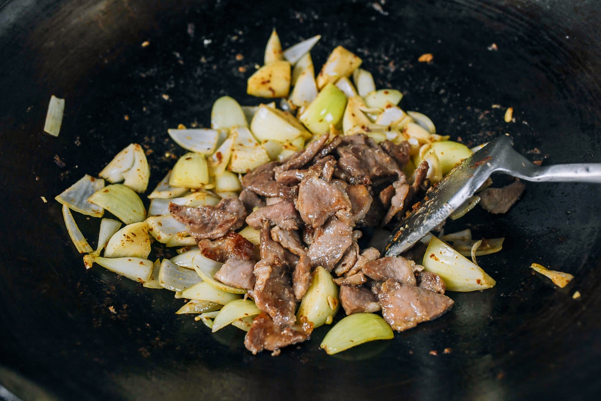 adding pork to onions in wok