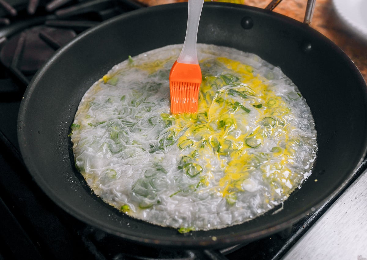 brushing gluten-free scallion pancake in pan with egg