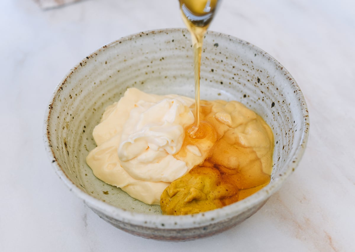 adding honey to honey mustard sauce ingredients in bowl