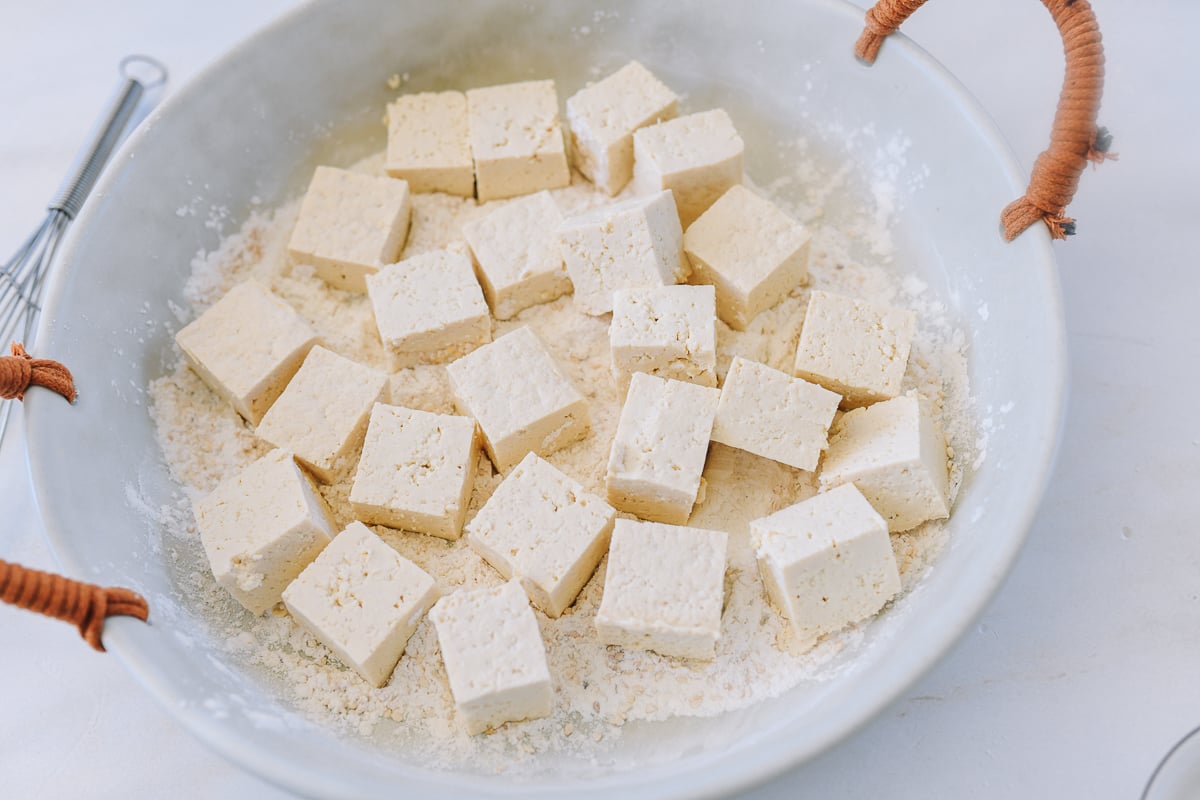 tofu cubes in bowl with cornstarch, sesame seeds, and seasonings