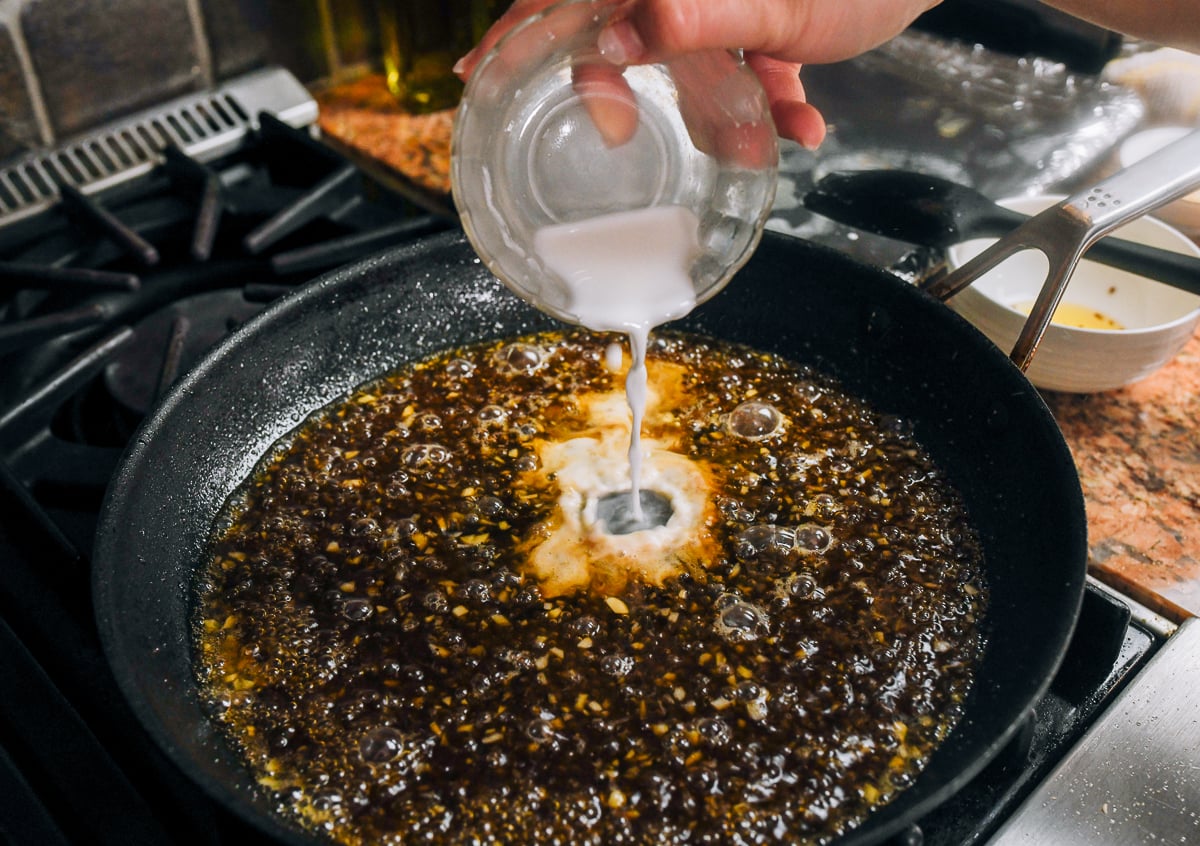 pouring cornstarch slurry in pan with sauce