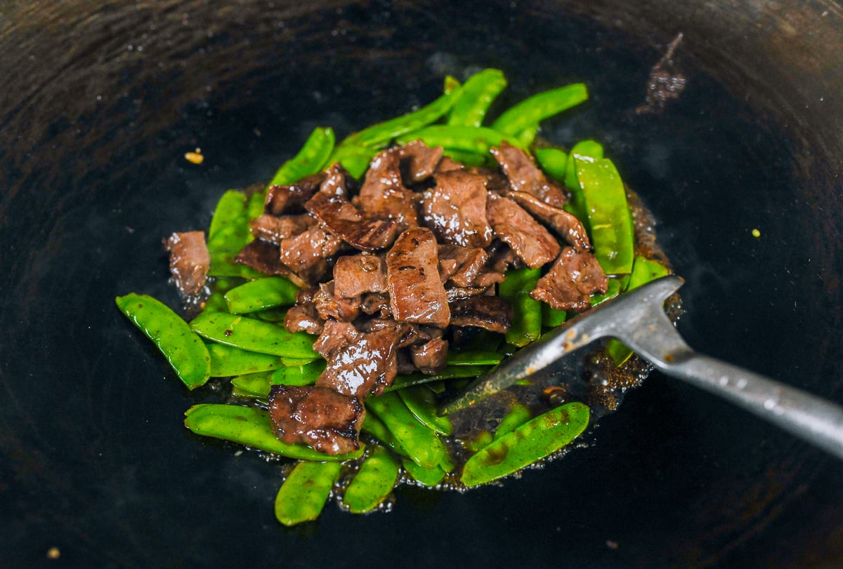 adding beef back to wok with snow peas