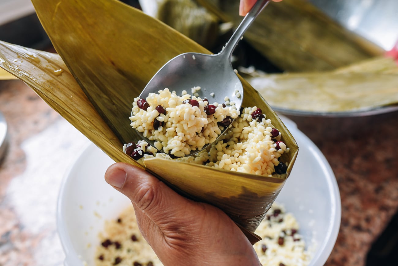 spooning rice and red bean mixture into bamboo leaf cone